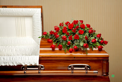 Red rose casket spray on a polished wood casket with white interior