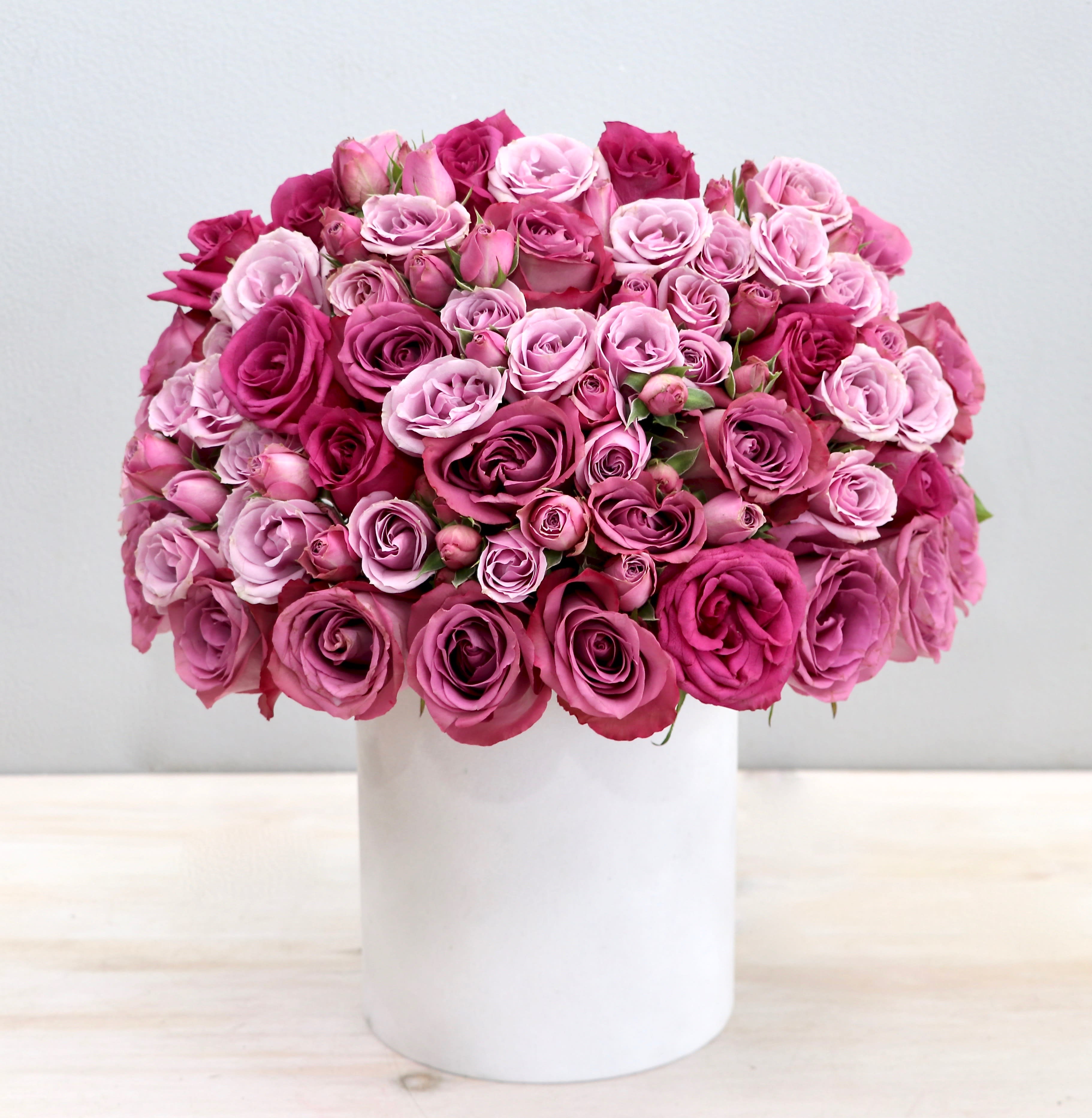 Dome-shaped arrangement of pink and magenta roses in a white cylinder vase