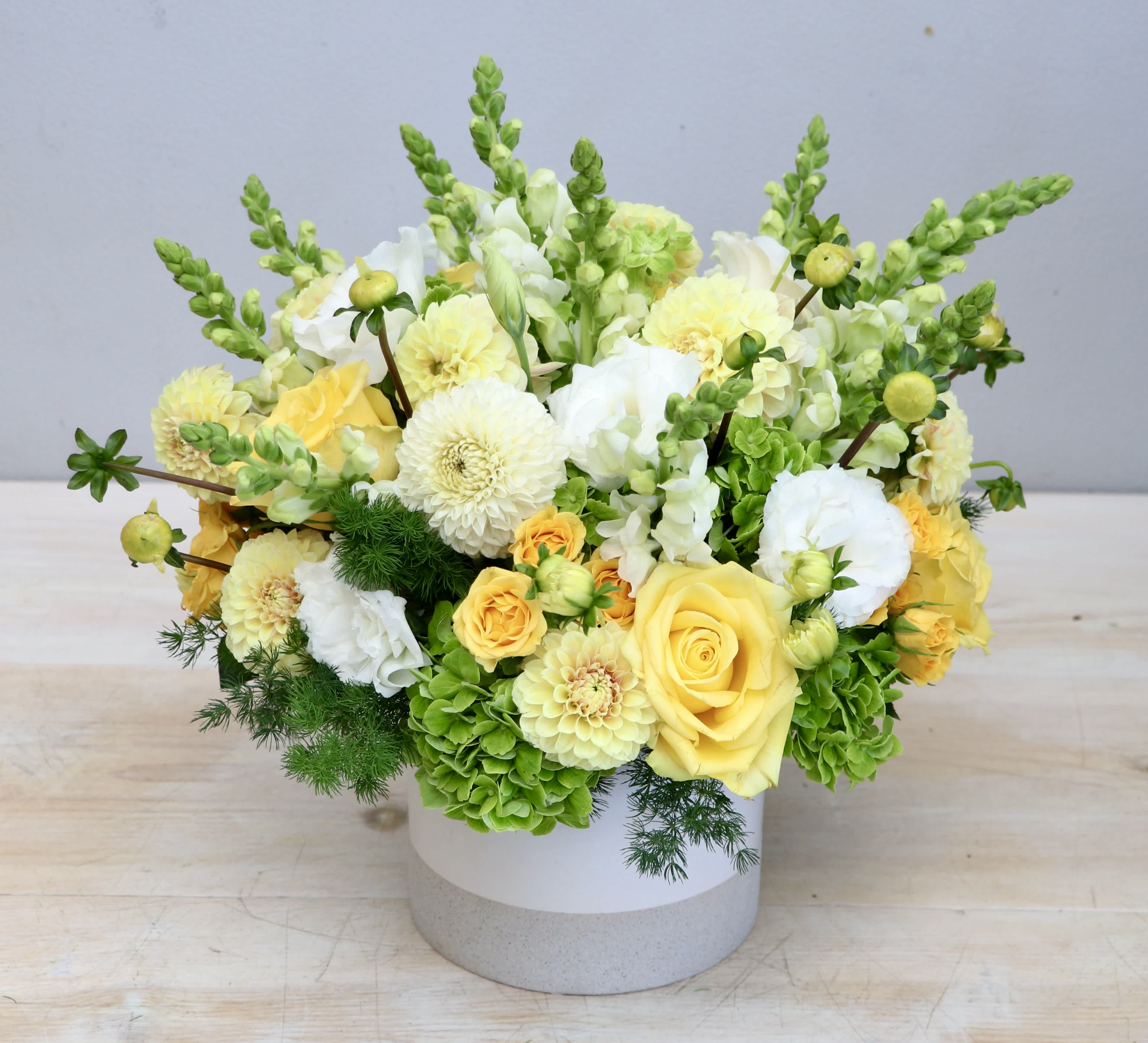 Low yellow and white flower arrangement with roses and snapdragons in a white ceramic cylinder vase
