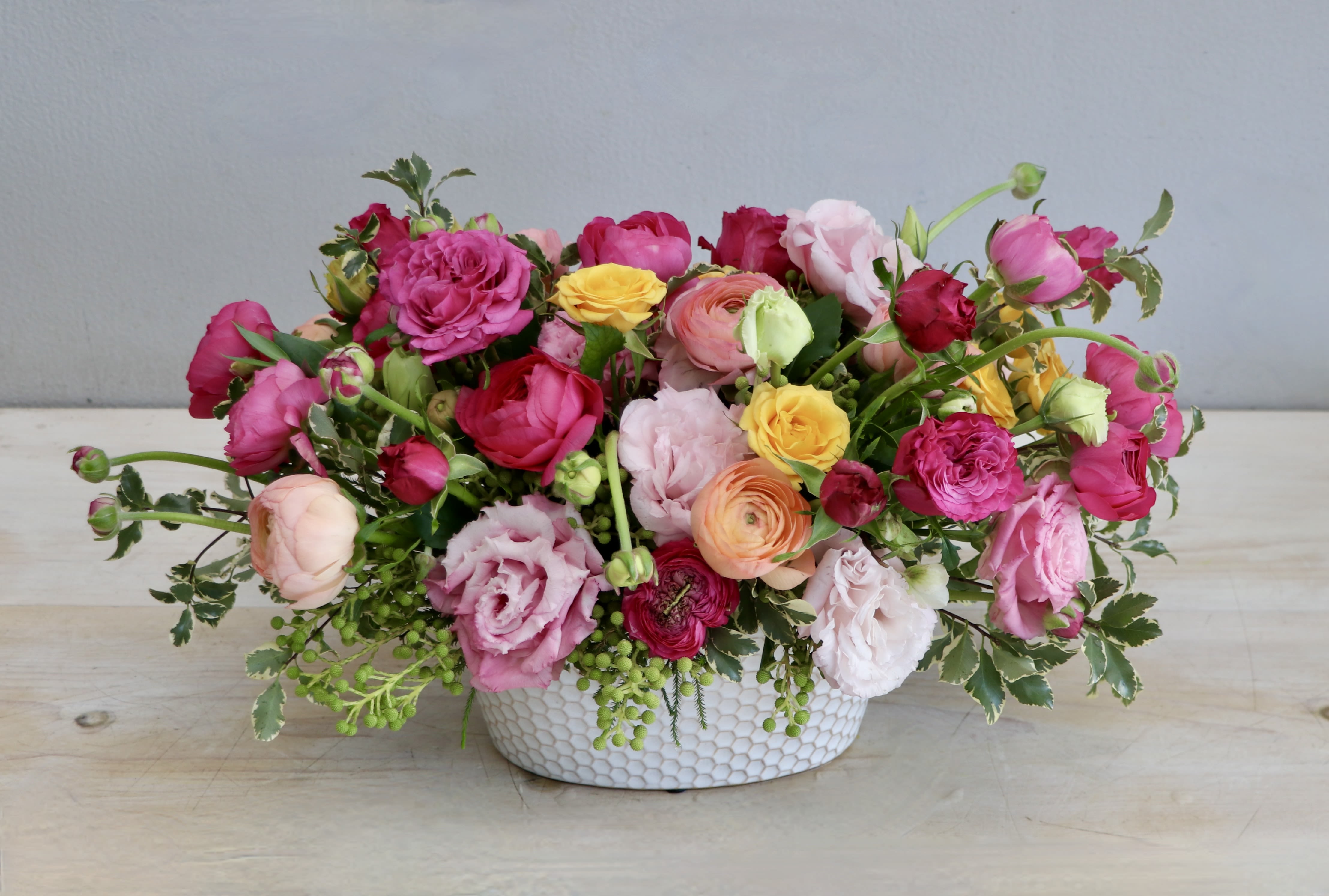 Low centerpiece of bright pink, yellow, and peach blooms in a white ceramic bowl.