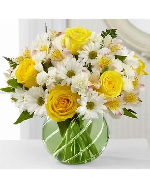 Sunlit Blooms - Designed to lift spirits and fill any day with sunshine joy, this bouquet beautifully captures the essence of springtime's return. The light green glass vase is spiral-wrapped with deep, hand-beveled cuts that add an extra bit of twinkle to its already sparkling surface. It makes a perfect base for the bouquet, an exuberant burst of bright and blissful blossoms that run the gamut from daisies to roses accented with subtle alstroemeria and mini carnations  