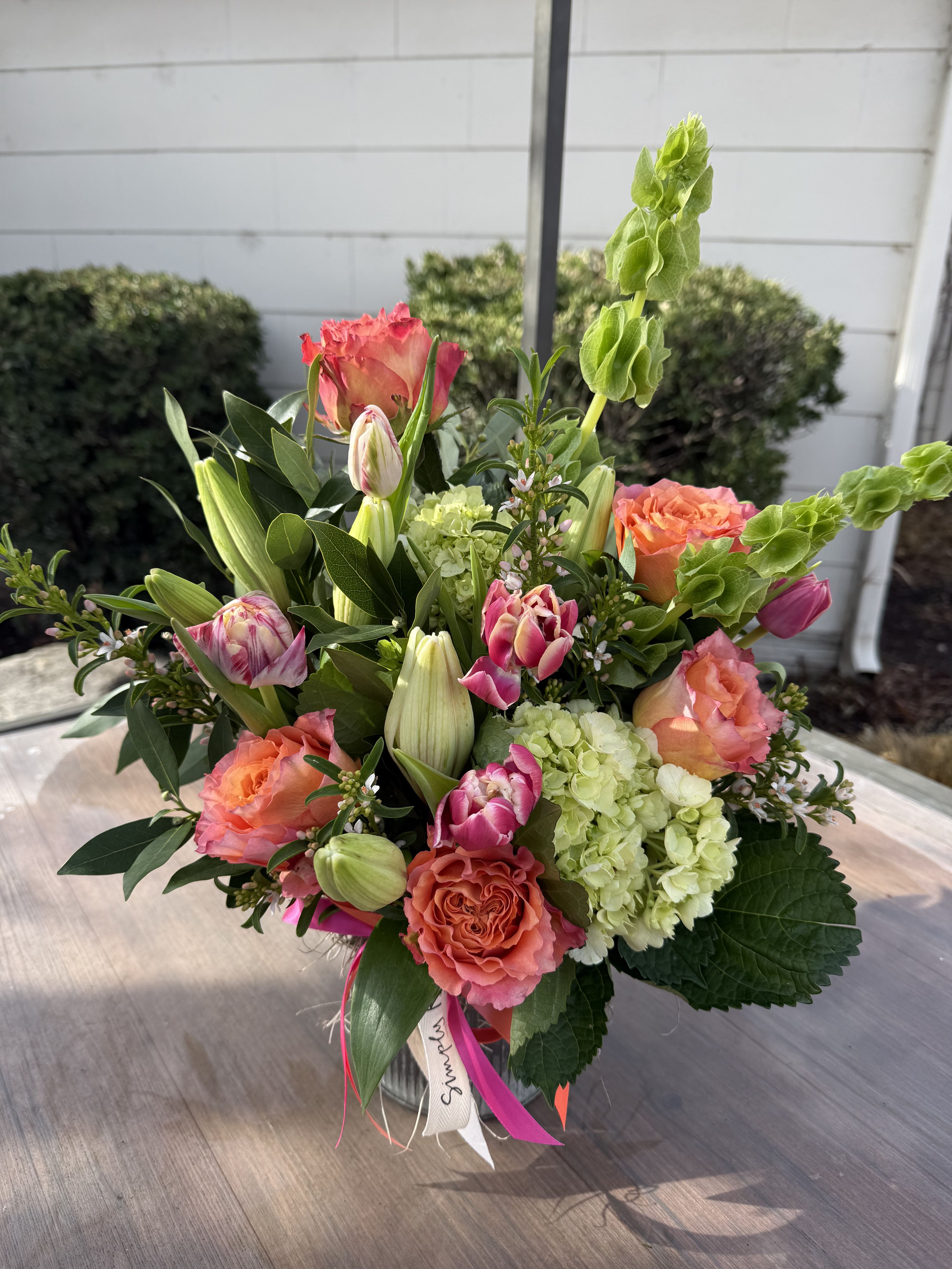 Mixed bouquet of coral roses, pink tulips, green hydrangeas, and lilies in a clear glass vase.