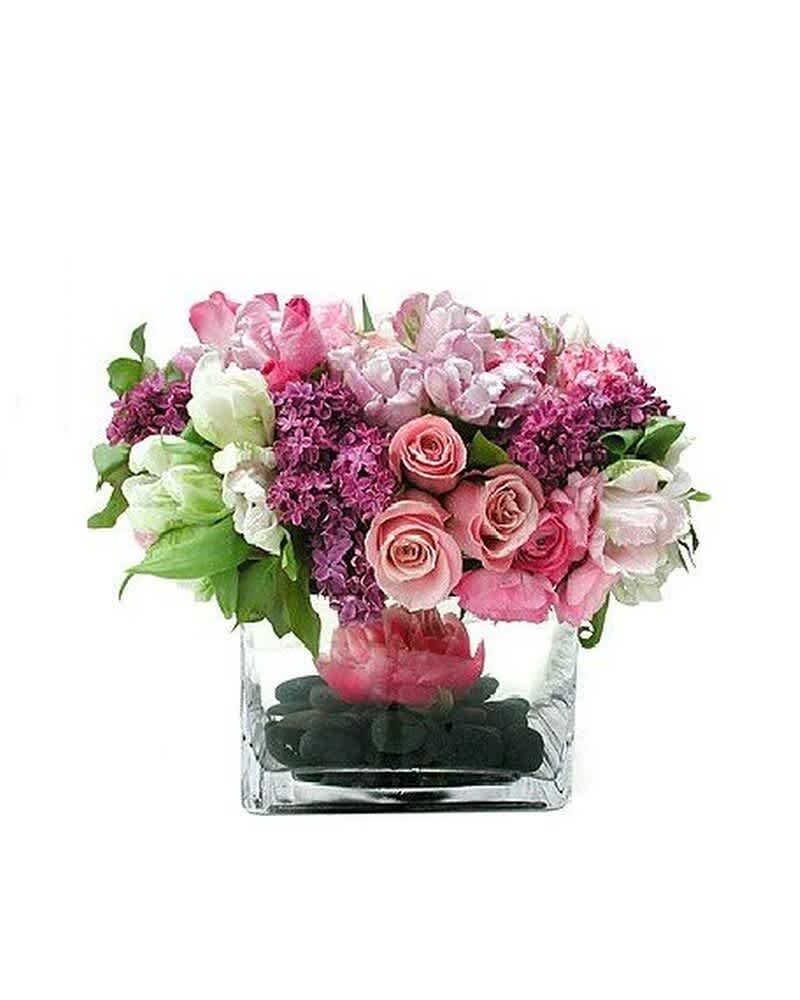 Low pink and purple flower arrangement in a clear square vase with black stones