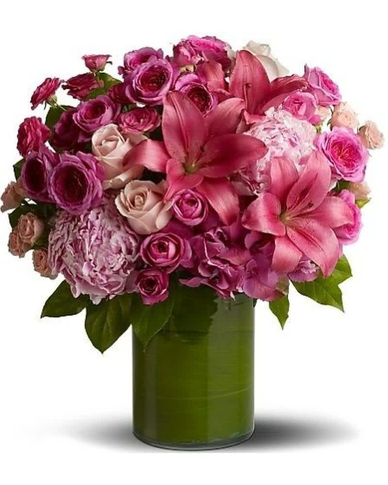 Pink lilies, roses, and hydrangeas arranged in a round bouquet in a green-lined glass cylinder vase