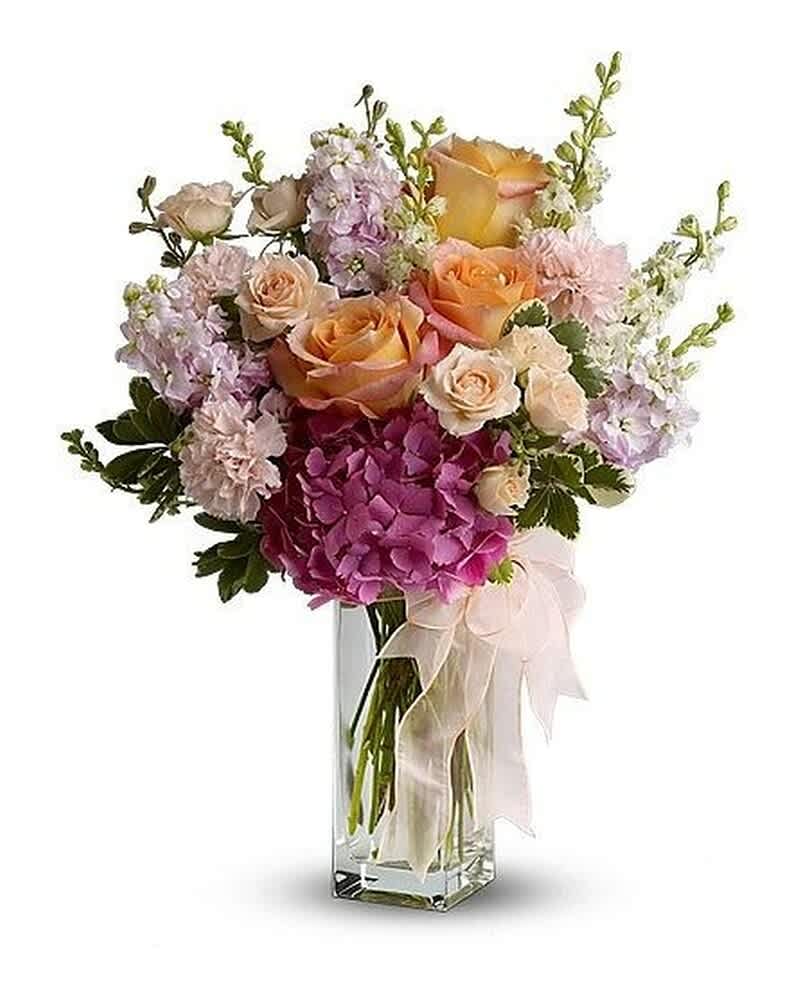 Tall vase arrangement of peach roses, pink hydrangea, pale carnations, and pastel flowers with a ribbon bow