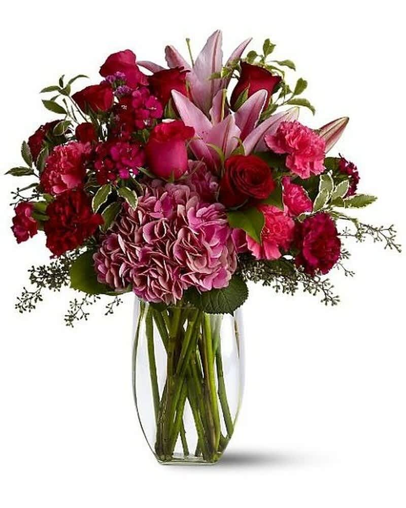 Mixed arrangement of pink lilies, roses, carnations, and hydrangea in a clear glass vase