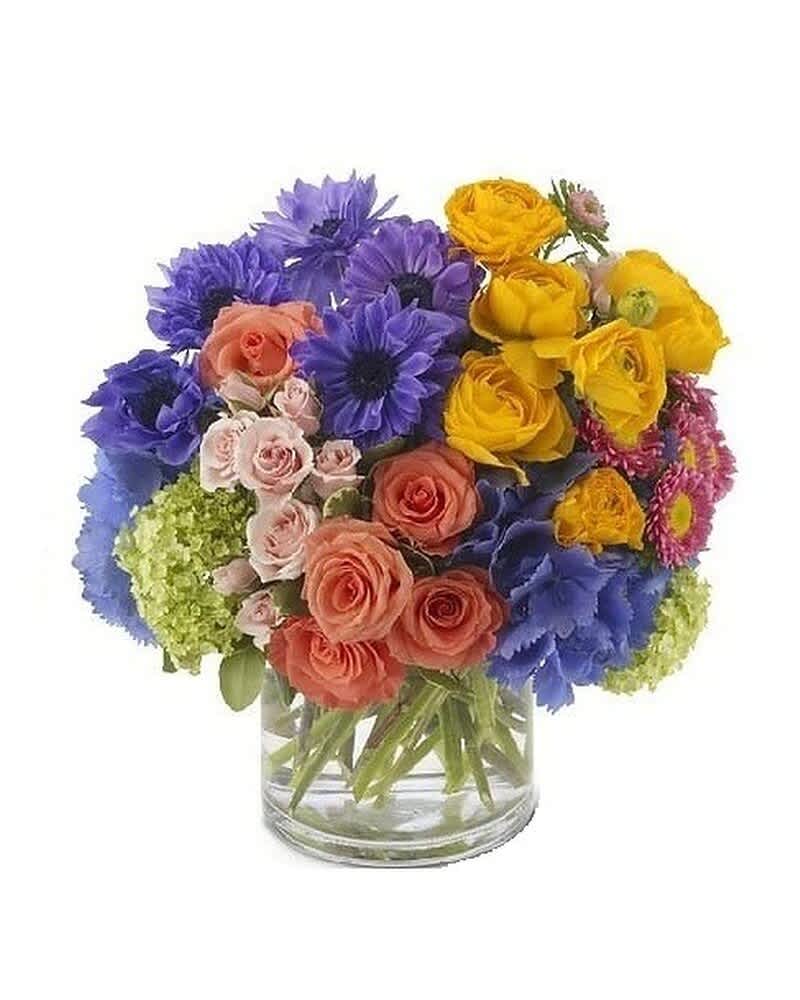 Bright mixed bouquet of blue daisies and peach and yellow roses in a clear glass cylinder vase