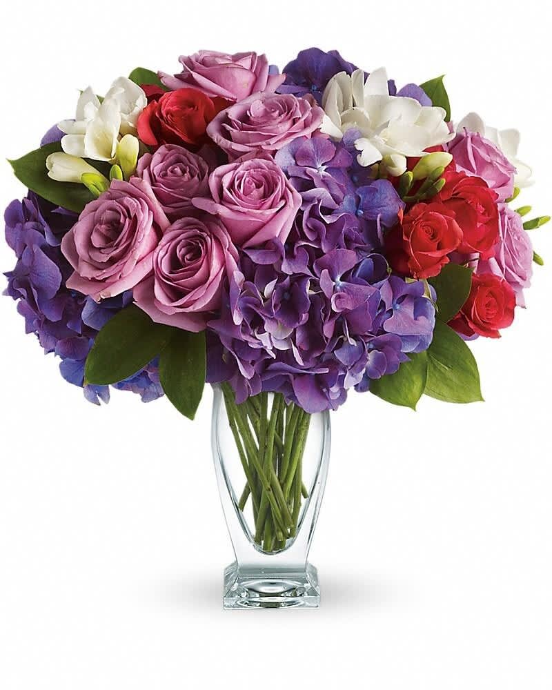 Arrangement of purple hydrangeas, lavender and red roses, and white freesia in a clear glass vase