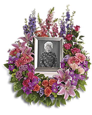 In Memoriam Wreath - Keep fond memories close to your heart with this lovely feminine floral wreath. It's perfect to surround a framed photo of the departed. Includes a multitude of flowers such as roses and carnations, along with pink gerberas, oriental lilies and snapdragons, purple orchids and asters, plus lavender delphinium. Green button spray chrysanthemums provide beautiful accents.Please note: Arrangement does not include picture frame. Orientation: One-Side