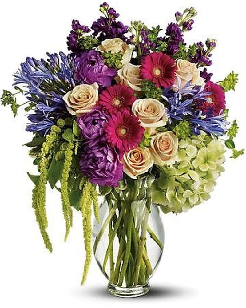 Tall mixed bouquet of purple, pink, cream, and green flowers in a clear glass vase
