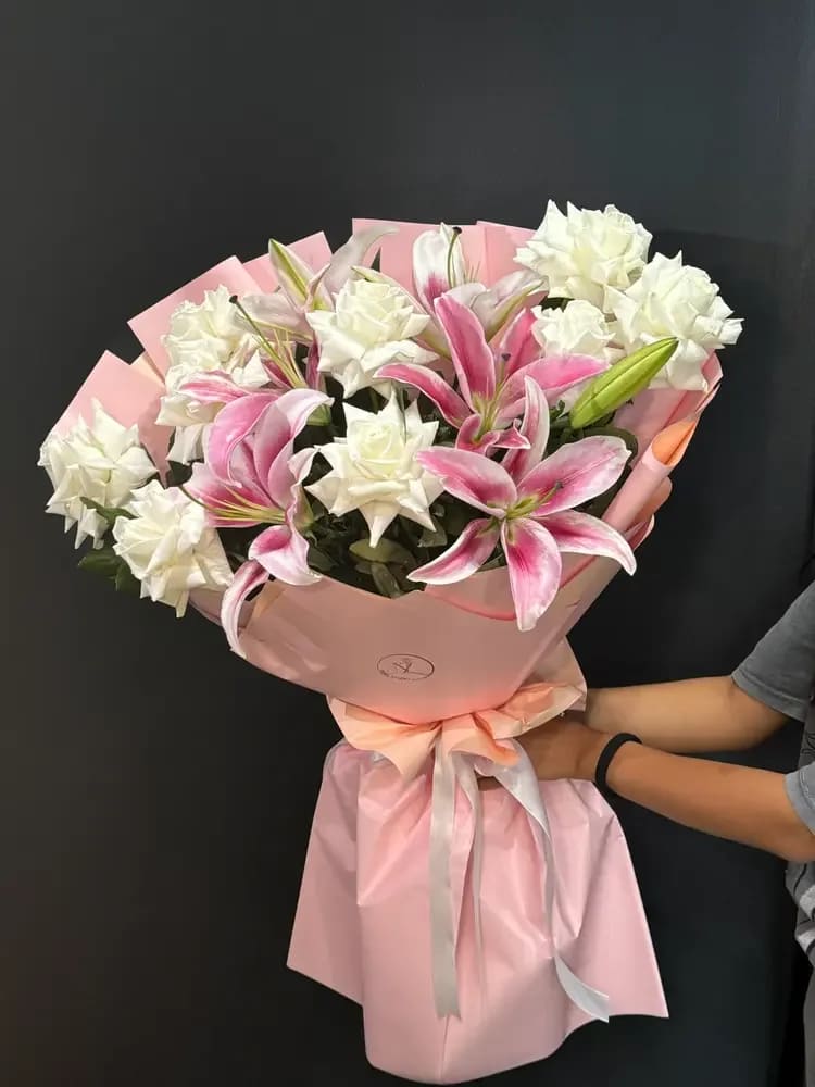Blush Lily Charm - Blush Lily Charm is a timeless and expressive bouquet that combines the elegance of white roses with the bold beauty of pink lilies. The soft contrast between creamy whites and rich pink tones creates a striking yet harmonious composition. Fragrant lilies bring depth and presence, while roses add a touch of classic romance. Designed in a full, rounded shape with delicate wrapping, this bouquet is perfect for birthdays, celebrations, or meaningful gestures. A beautiful choice for those who appreciate classic floral design with a vibrant and modern twist.
