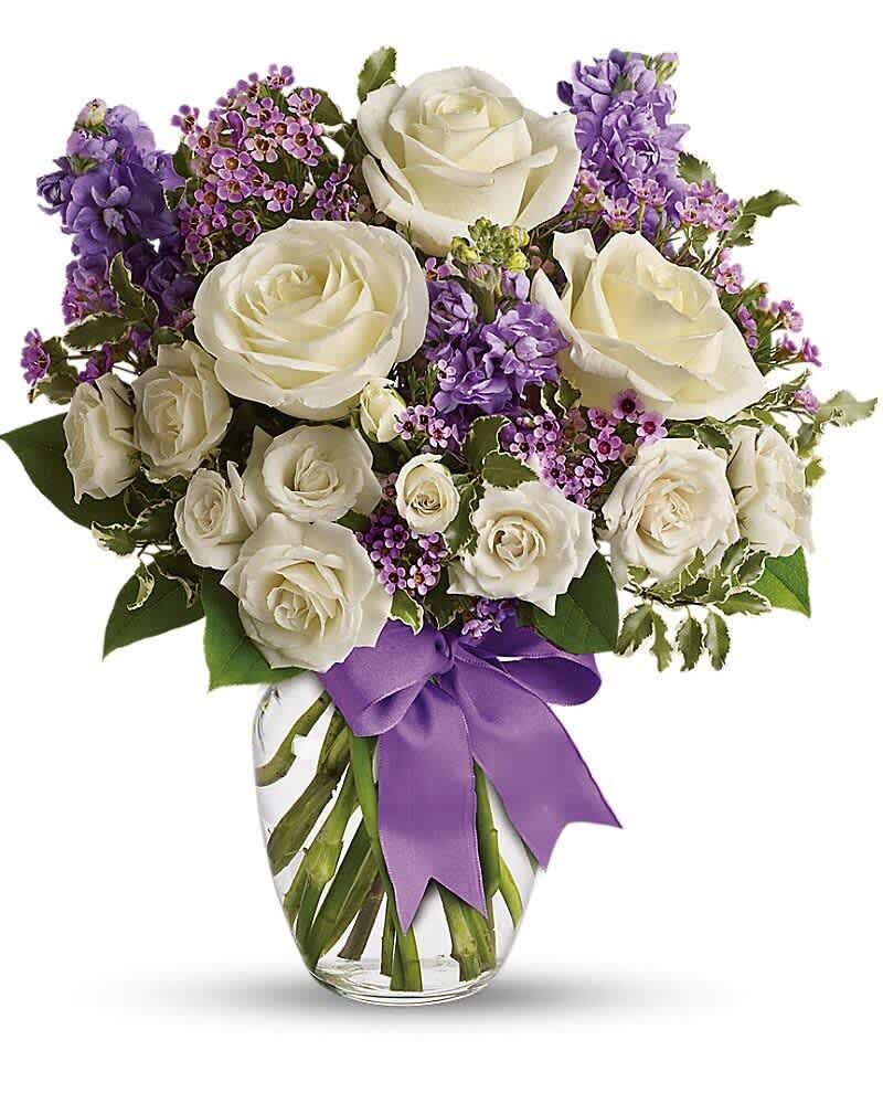 Arrangement of white roses and purple flowers in a clear glass vase with a purple ribbon.