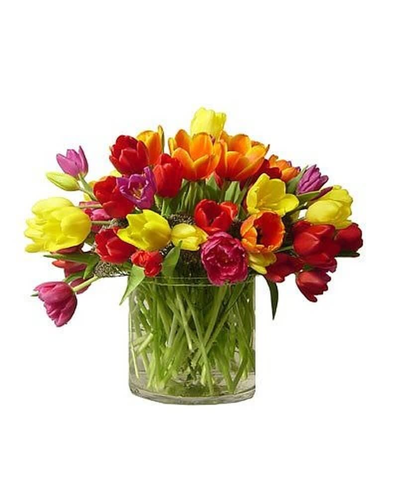 Low glass vase filled with bright mixed tulips in red, yellow, orange, and pink.