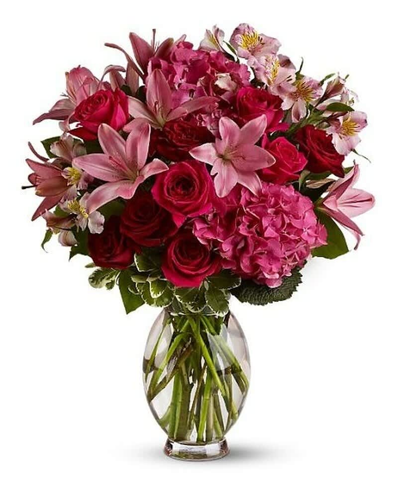 Arrangement of red roses, pink lilies, hydrangeas, and alstroemeria in a clear glass vase