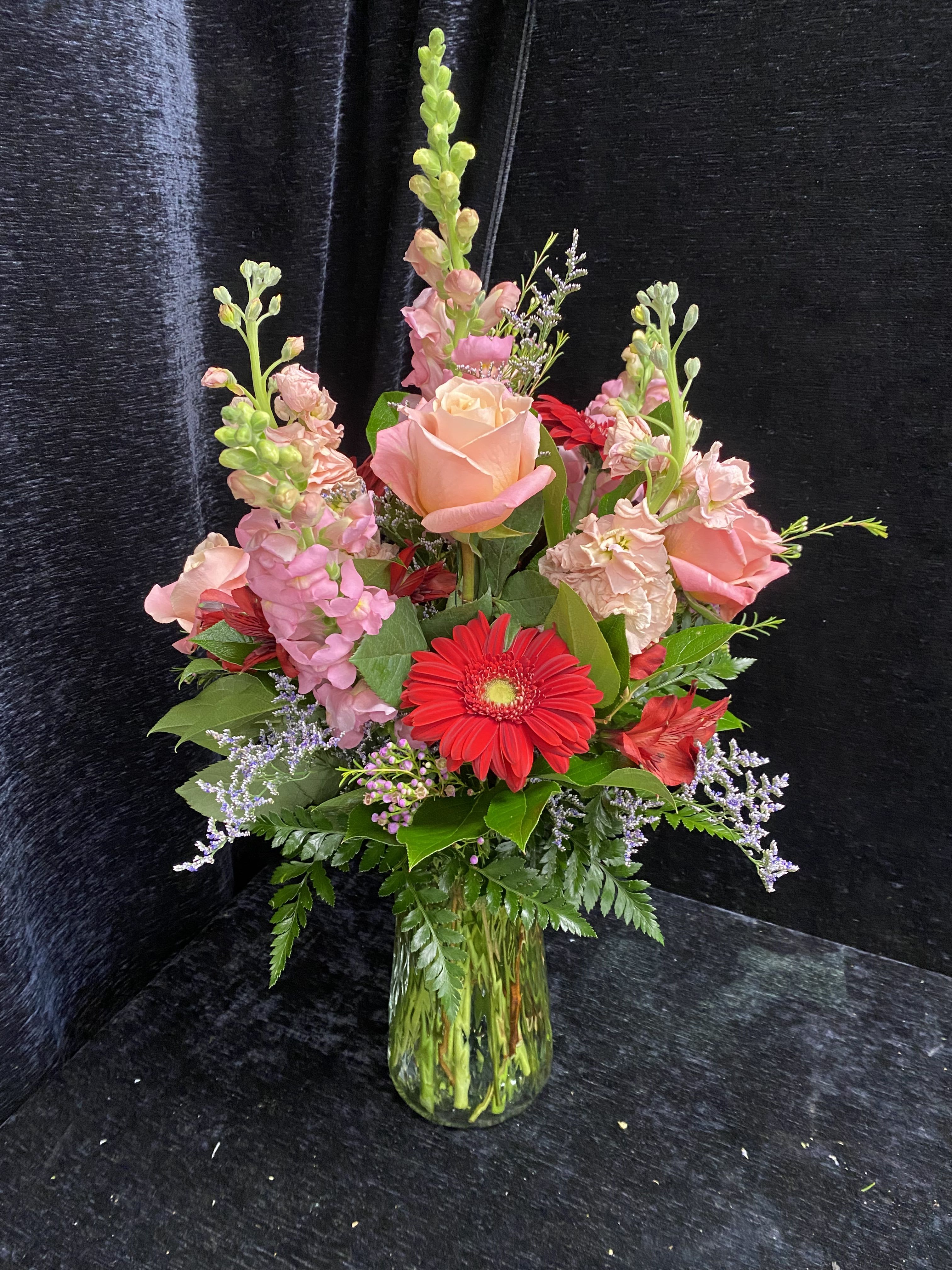 Cat Mom - A tall, joyful arrangement perfect for the cat-loving mom who deserves something playful and elegant - this flower arrangement is ideal for Mother's Day, an anniversary, or a warm "thinking of you" surprise. The mix of red, pink, lavender, and peach reads like a cheerful hug: vivid red gerbera daisies deliver bold pops of color while blush-pink roses and pink snapdragons lift the composition with romantic height and softness.  All of these blooms are rated cat safe by the ASPCA for a worry-free gift. Place in fresh water, trim stems if needed, and refresh the water every few days to keep blooms looking their best.