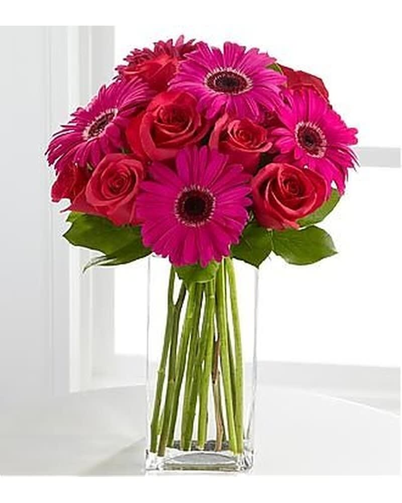 Bright pink gerbera daisies and red roses in a tall rectangular glass vase