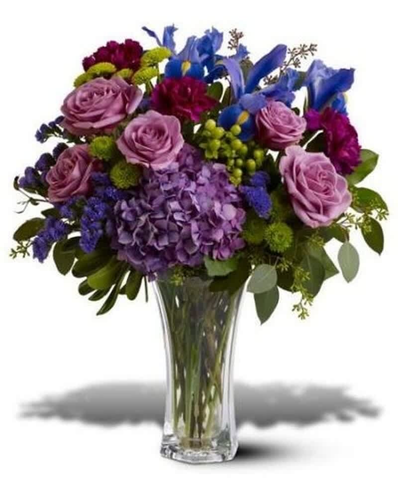 Purple and blue mixed flower arrangement with roses, hydrangea, and irises in a clear glass vase