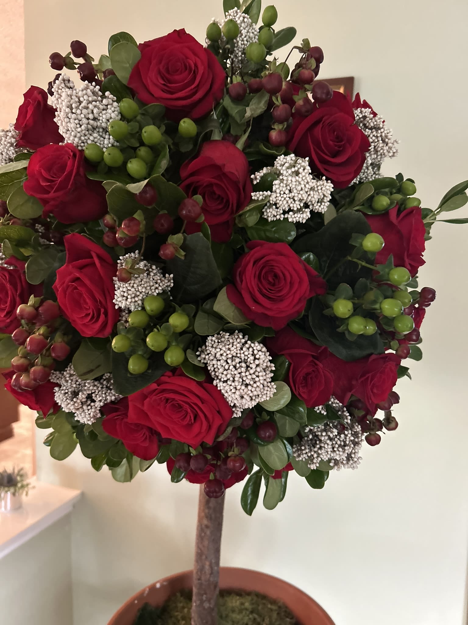 Christmas Topiary tree - An irresistibly fairy tale of a piece. A floral topiary made with real wood and terra cotta pot. Rose, and red and green berries complete the look. Can be made with appropriate glass ornaments in silver or gold. 3 pictured with ornamental balls