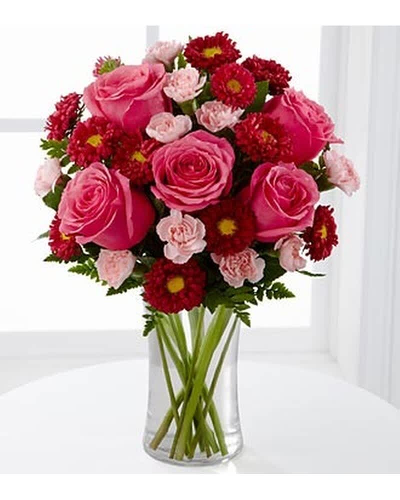 Pink roses with red mums and light pink carnations arranged in a clear glass vase.