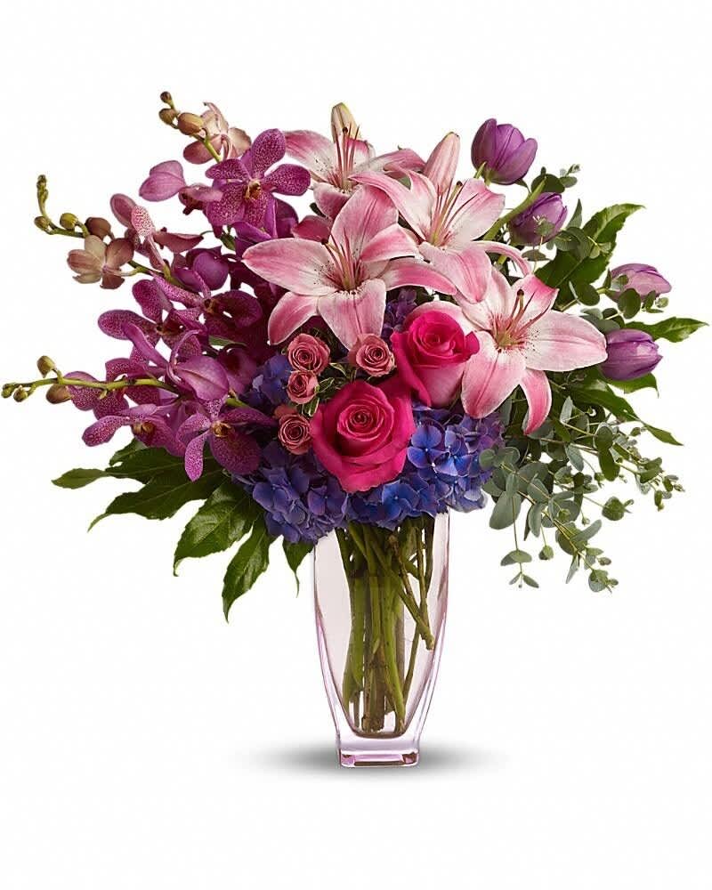 Tall vase of pink lilies, hot pink roses, purple orchids, tulips, and blue hydrangeas.