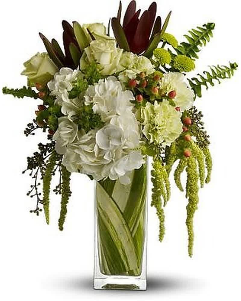 Tall arrangement of white hydrangeas, roses, and green flowers in a clear rectangular glass vase