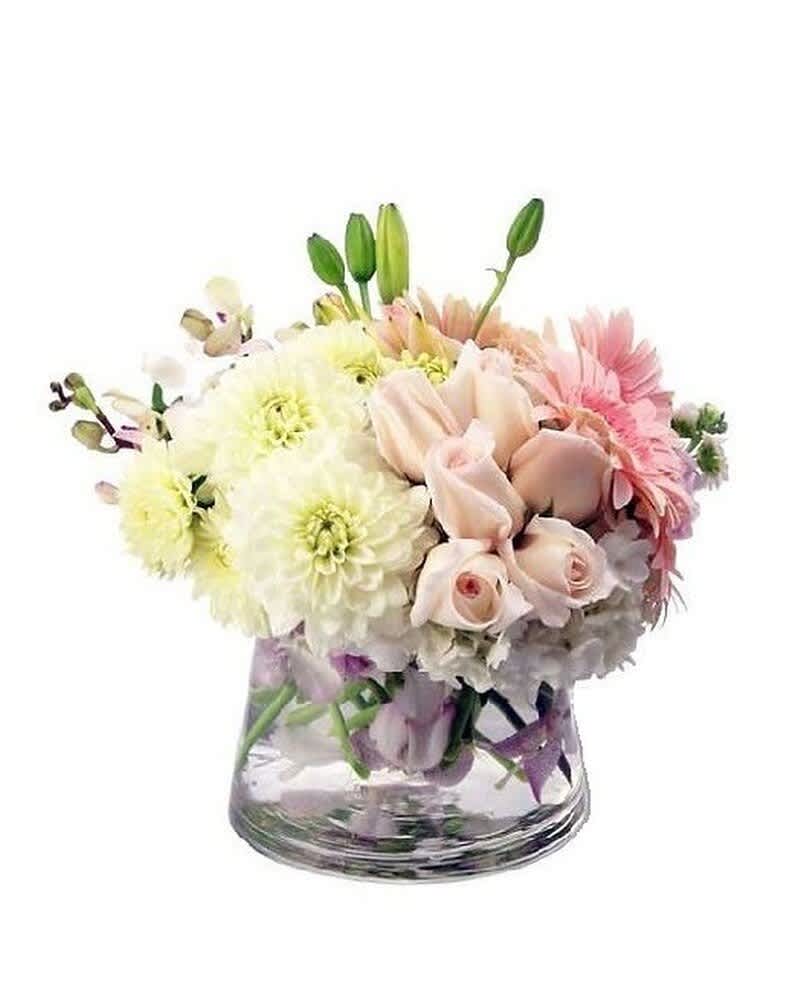 Low pastel arrangement of white dahlias, pink roses, and gerbera daisies in a clear glass vase
