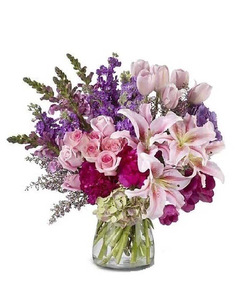 Mixed bouquet of pink lilies, roses, tulips, and purple flowers in a clear glass vase