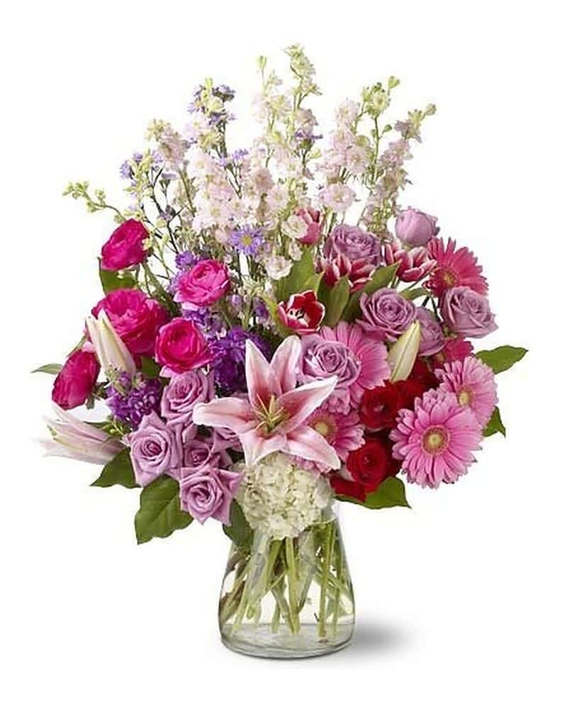 Mixed bouquet of pink lilies, roses, gerberas, and purple blooms in a clear glass vase