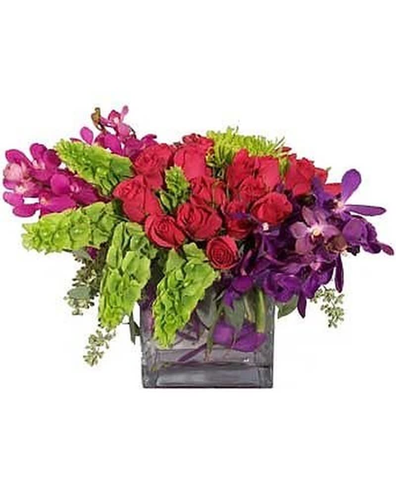 Low arrangement of red roses, green bells of Ireland, and purple orchids in a glass cube vase