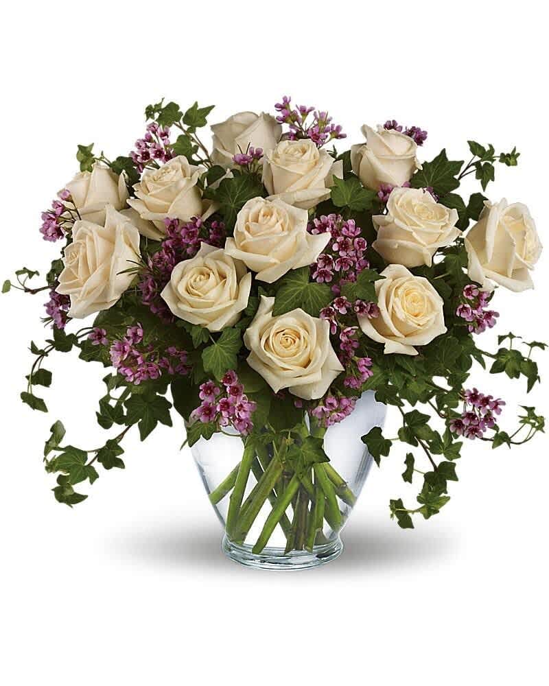 Arrangement of cream roses with small purple flowers and trailing ivy in a clear glass vase