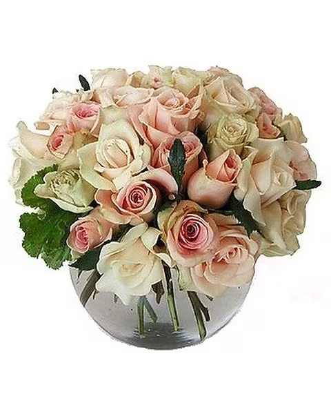 Low round arrangement of blush and cream roses in a clear glass bowl vase