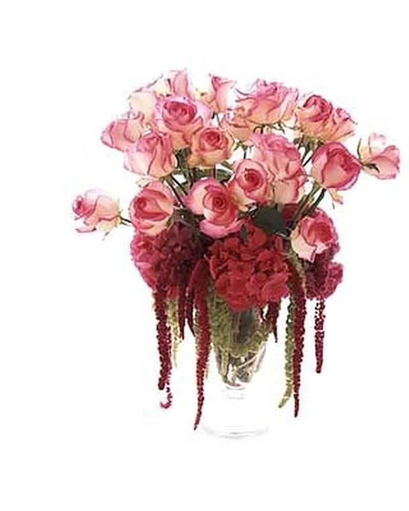 Tall arrangement of pink roses with dark red blooms and trailing accents in a clear glass vase