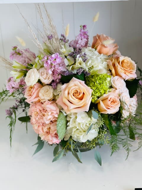 Shimmer - A delicate and elegant arrangement in soothing pastel hues, featuring classic roses, lush hydrangeas, spray roses, fragrant stock, and complemented by unique dry elements for added texture. This soft and timeless design exudes a sense of serenity, perfect for any occasion that calls for beauty and grace.