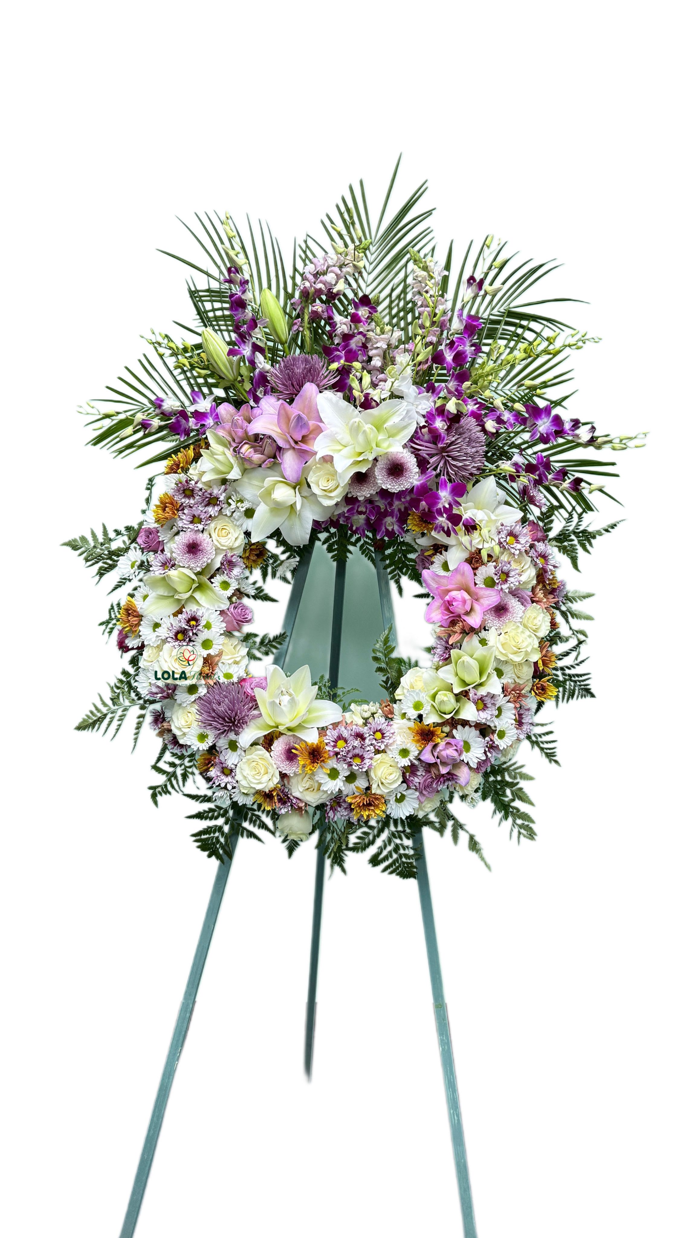 Eternal Peace 02 - A large circular standing wreath arranged for moments of remembrance, this funeral flower arrangement brings a calm, dignified presence to a memorial or graveside service. The design reads as a sympathy wreath and condolence tribute-made to honor a life and offer comfort to the person you're remembering and those who gather for the service.  Densely set on a tall metal easel, the ring is layered with white and pastel blooms: white lilies, roses, chrysanthemums and daisies mingle with soft pink and pale yellow accents for a gentle, peaceful palette. Clusters of rich purple dendrobium orchids sweep up one side into a taller spray, providing dramatic contrast and an elegant vertical line that lifts the composition. The wreath is substantial in scale and intended for standing display.  Perfect for memorial services, funeral homes, or a graveside farewell, this arrangement speaks of respect and consolation-she'll feel truly honored when it's chosen in their memory. The metal easel is included for immediate standing presentation; please contact us with service details for timing and delivery to the venue.