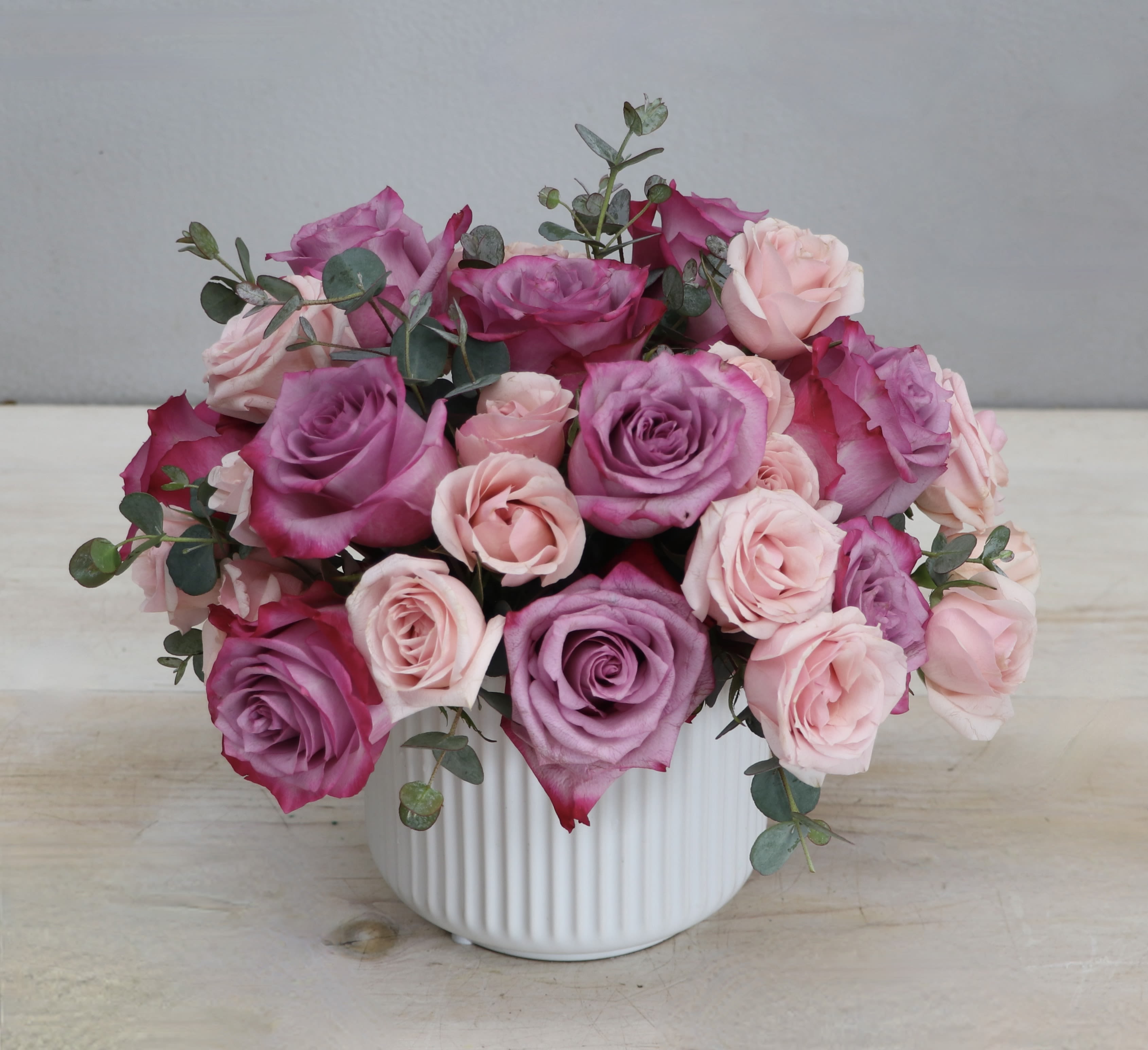 Low arrangement of mauve and light pink roses in a white ribbed ceramic vase