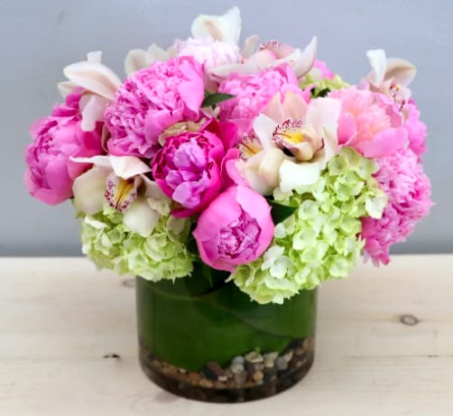 Compact arrangement of pink peonies, white orchids, and green hydrangeas in a glass vase