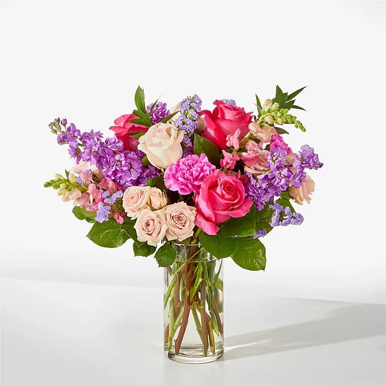 Pink and lavender mixed flower arrangement with roses and carnations in a clear glass vase