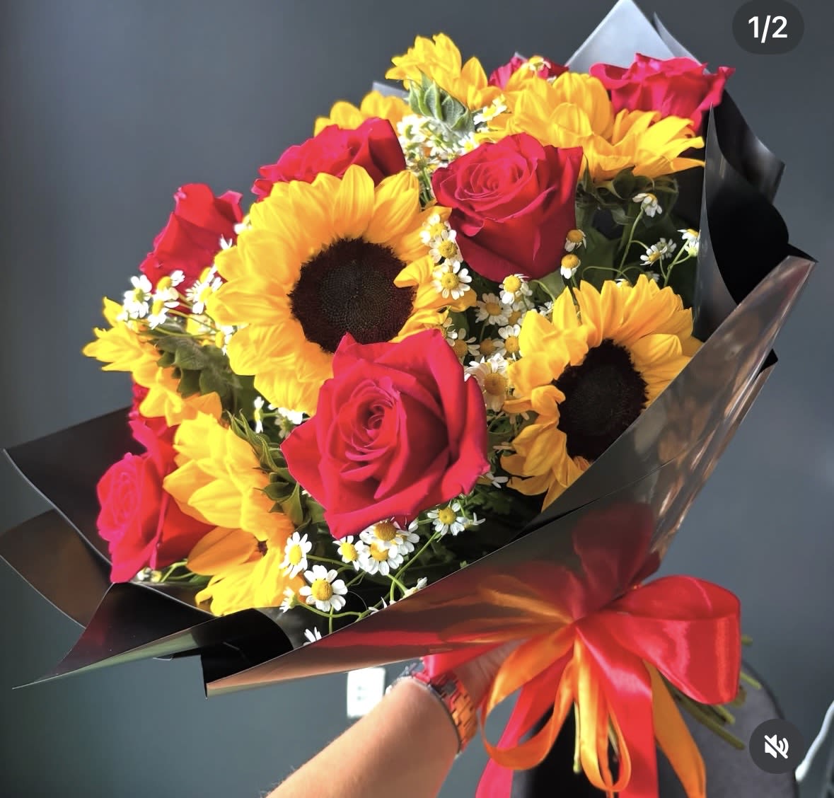 Sunlit Passion - This striking bouquet combines radiant sunflowers with classic red roses, accented by delicate chamomile for a soft, natural touch. The contrast of bold yellow and deep red creates a powerful yet joyful composition, perfect for celebrating love, happiness, and unforgettable moments. Wrapped in sleek black paper with a vibrant ribbon, this design feels both modern and expressive — ideal for gifting when you want to make a statement.