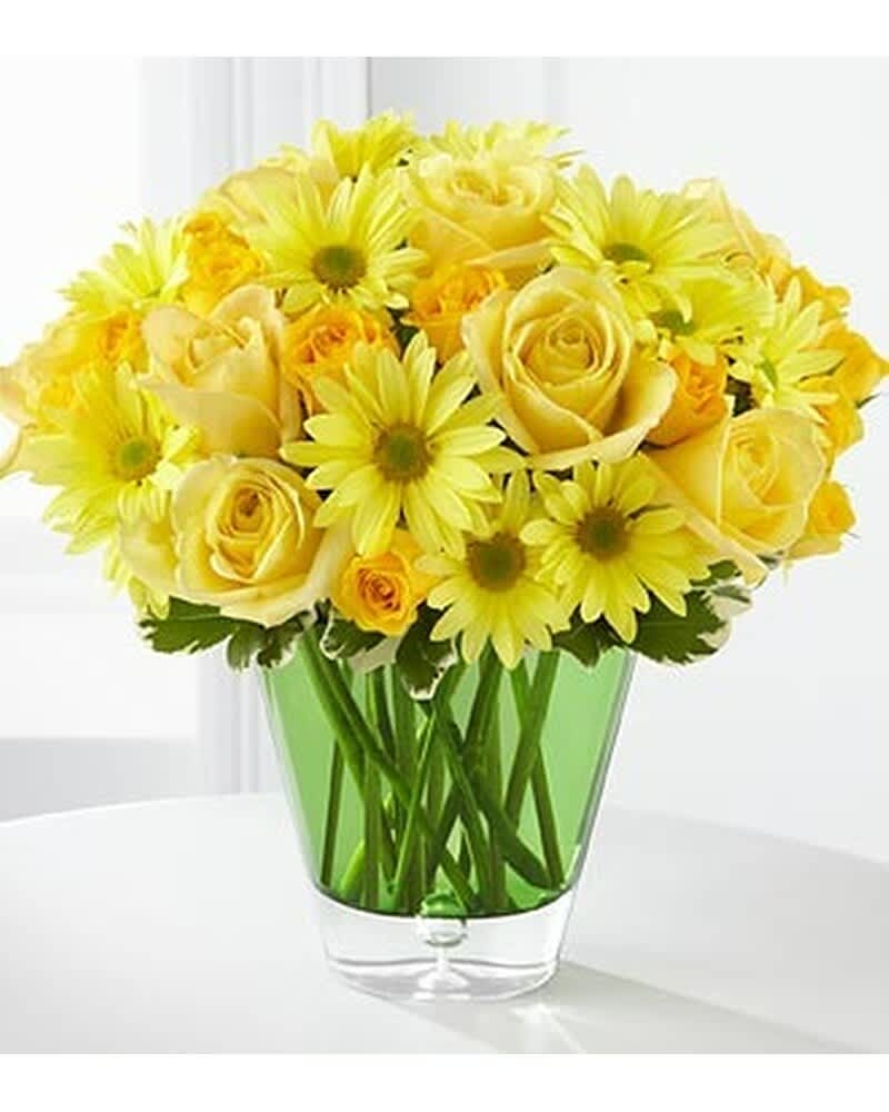 Yellow roses and daisy-style flowers arranged in a clear vase with green glass lining