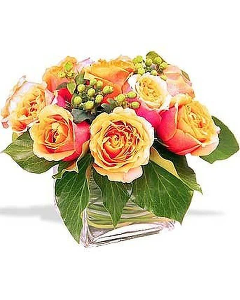 Short arrangement of orange and yellow roses with berries in a clear glass cube vase