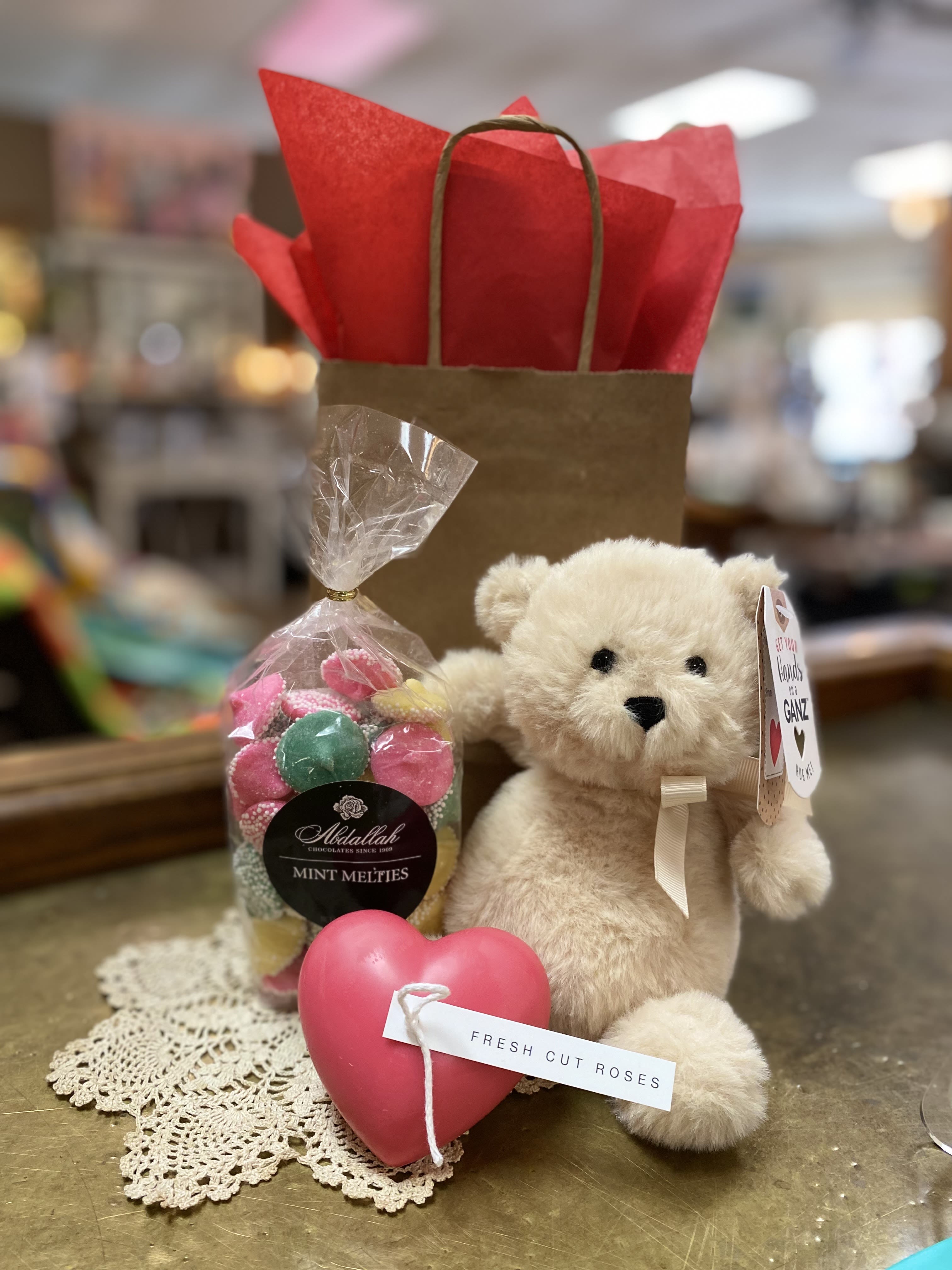 Gift set with teddy bear, bag of candies, and pink heart on a lace doily