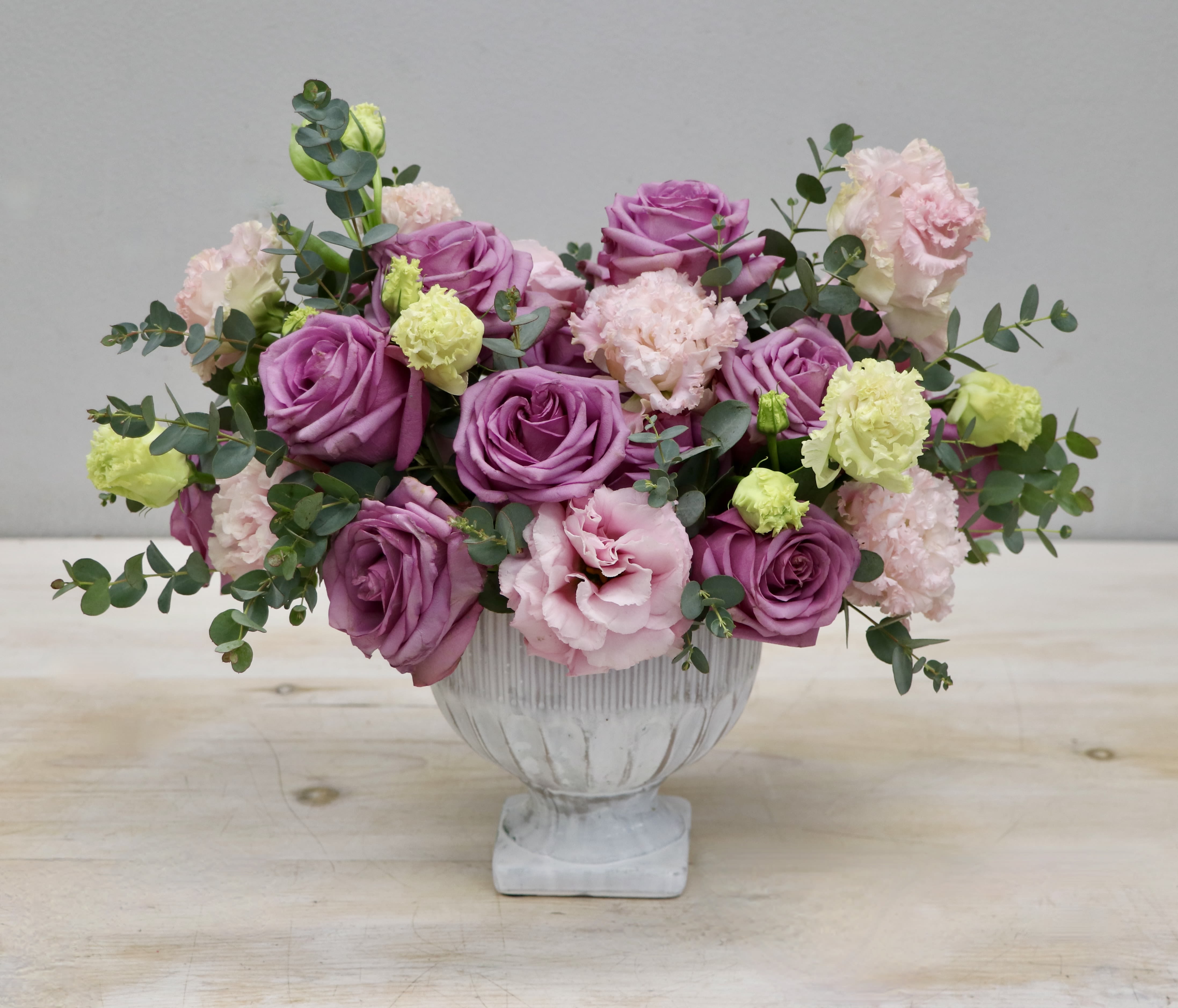Low centerpiece of purple roses with pale pink and green carnations in a white footed bowl.