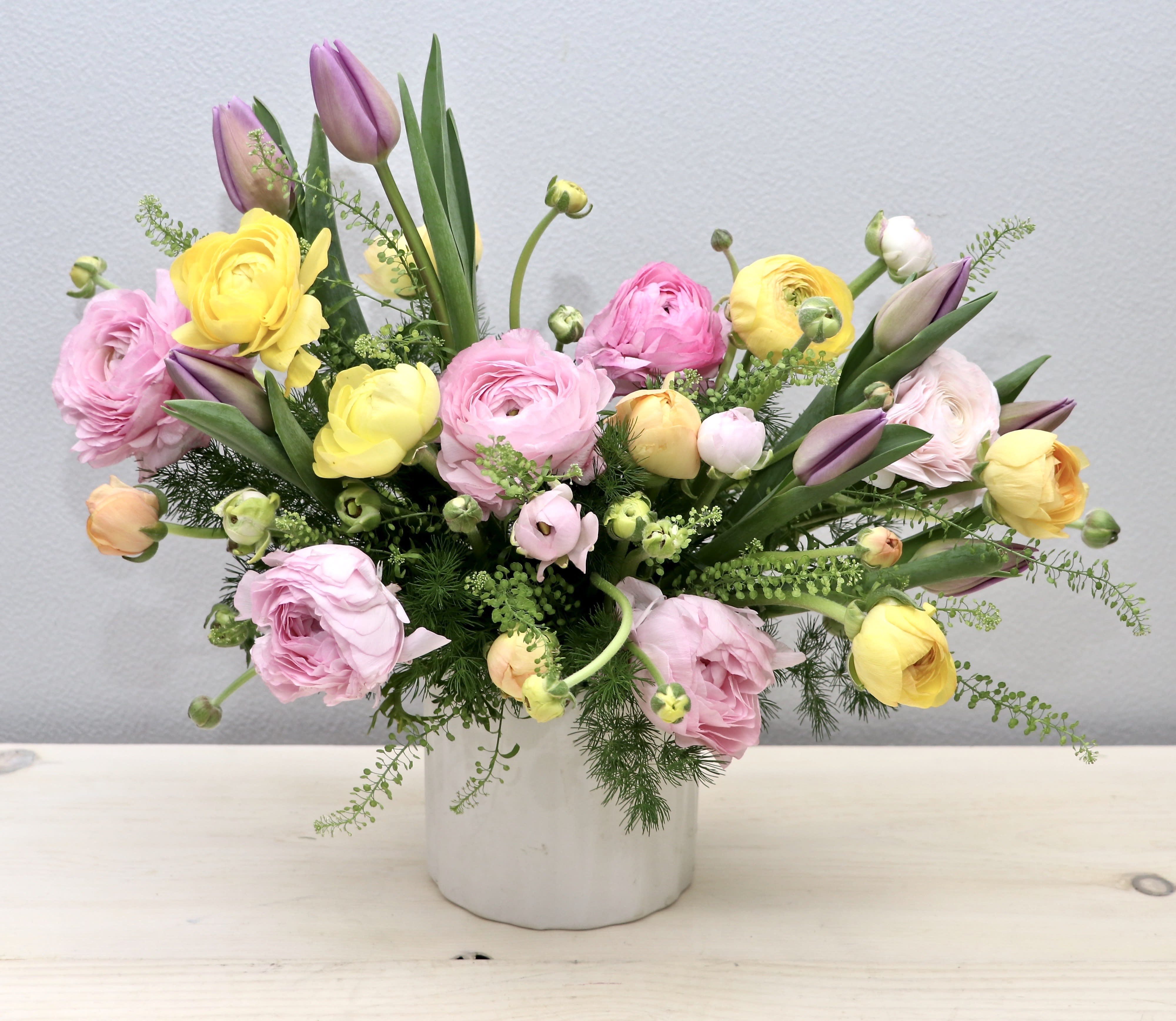 Pastel arrangement of pink, yellow and lavender blooms with tulips in a white ceramic vase