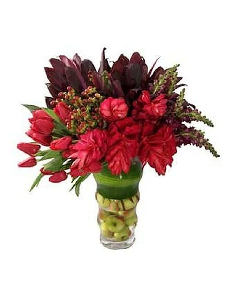 Tall arrangement of red flowers in a clear vase filled with stacked green apples