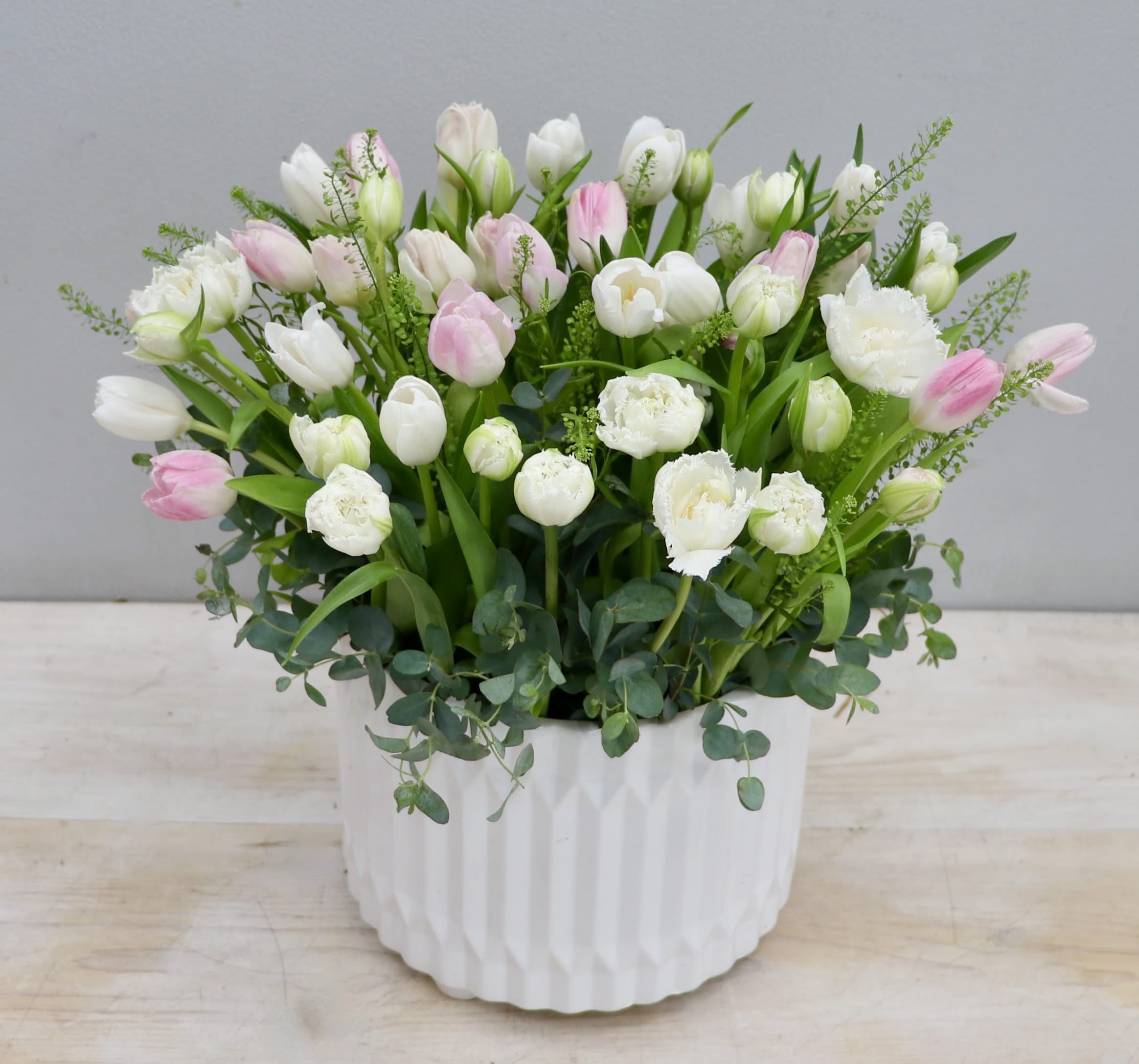 White and pale pink tulips in a round white textured ceramic pot