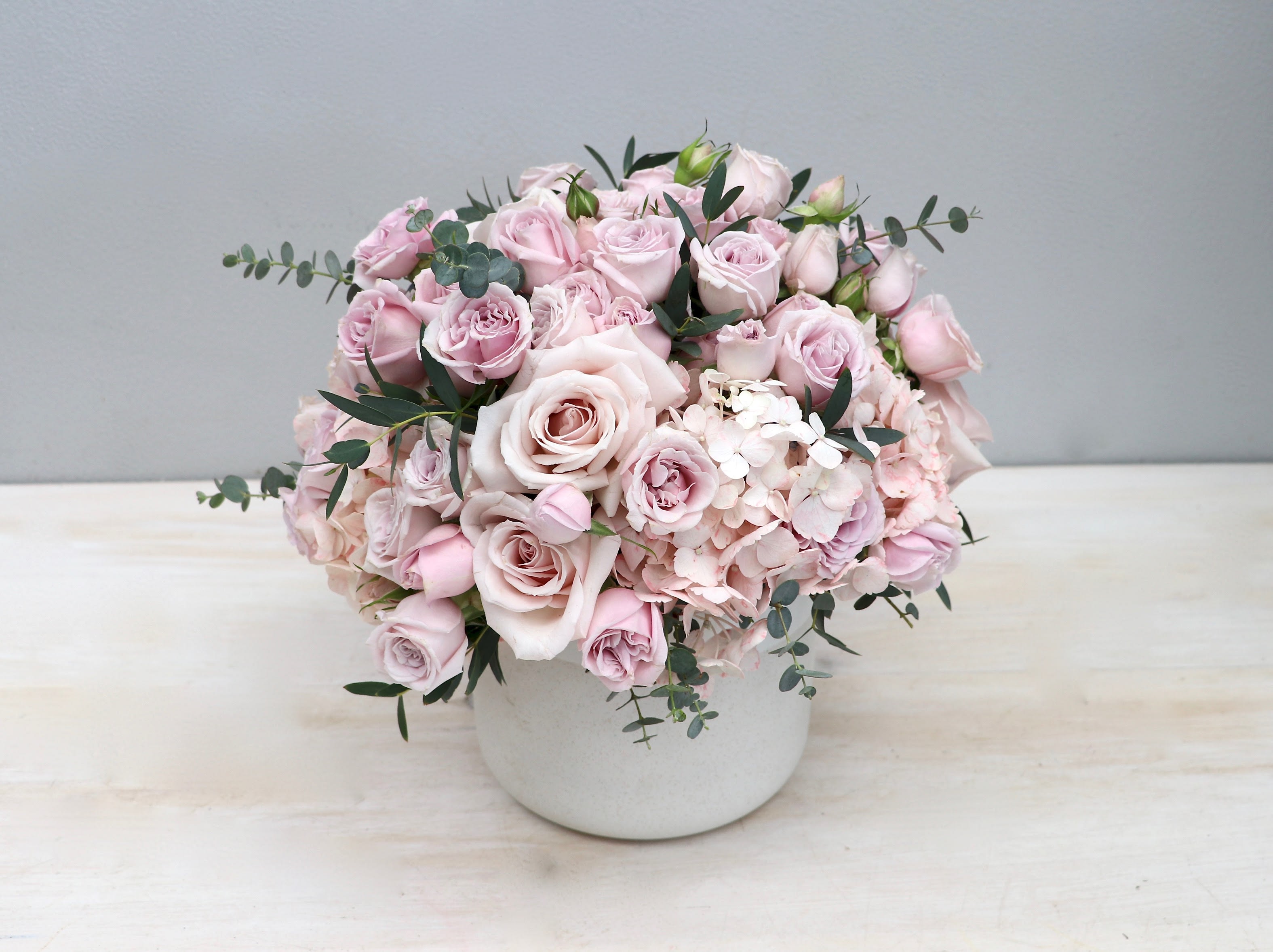 Compact arrangement of pale pink roses and hydrangeas in a white ceramic pot