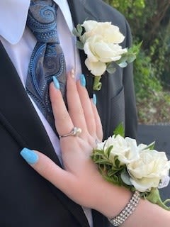 Neutral wrist corsage and boutonniere - A pair designed for timeless wedding coordination: a white rose wrist corsage and matching white rose boutonniere that read classic and refined against dark suits and formal dresses. Perfect for weddings and other formal celebrations, this neutral wrist corsage and boutonniere set creates a quiet, romantic statement-she'll feel put-together and cherished, and he'll wear a complementary accent that ties both looks together.  Each piece features small clustered white roses that sit prominently on a wrist bracelet and a suit lapel, the soft white petals contrasted against black or navy fabrics and paired with dress-shirt and necktie details for a polished finish. The wrist corsage secures on a bracelet-style band for comfortable wear; the boutonniere is sized for a men's suit jacket lapel. Together they're ideal for couples, attendants, or anyone in the wedding party who wants coordinated, understated florals that photograph beautifully and stay elegant through the ceremony and reception.