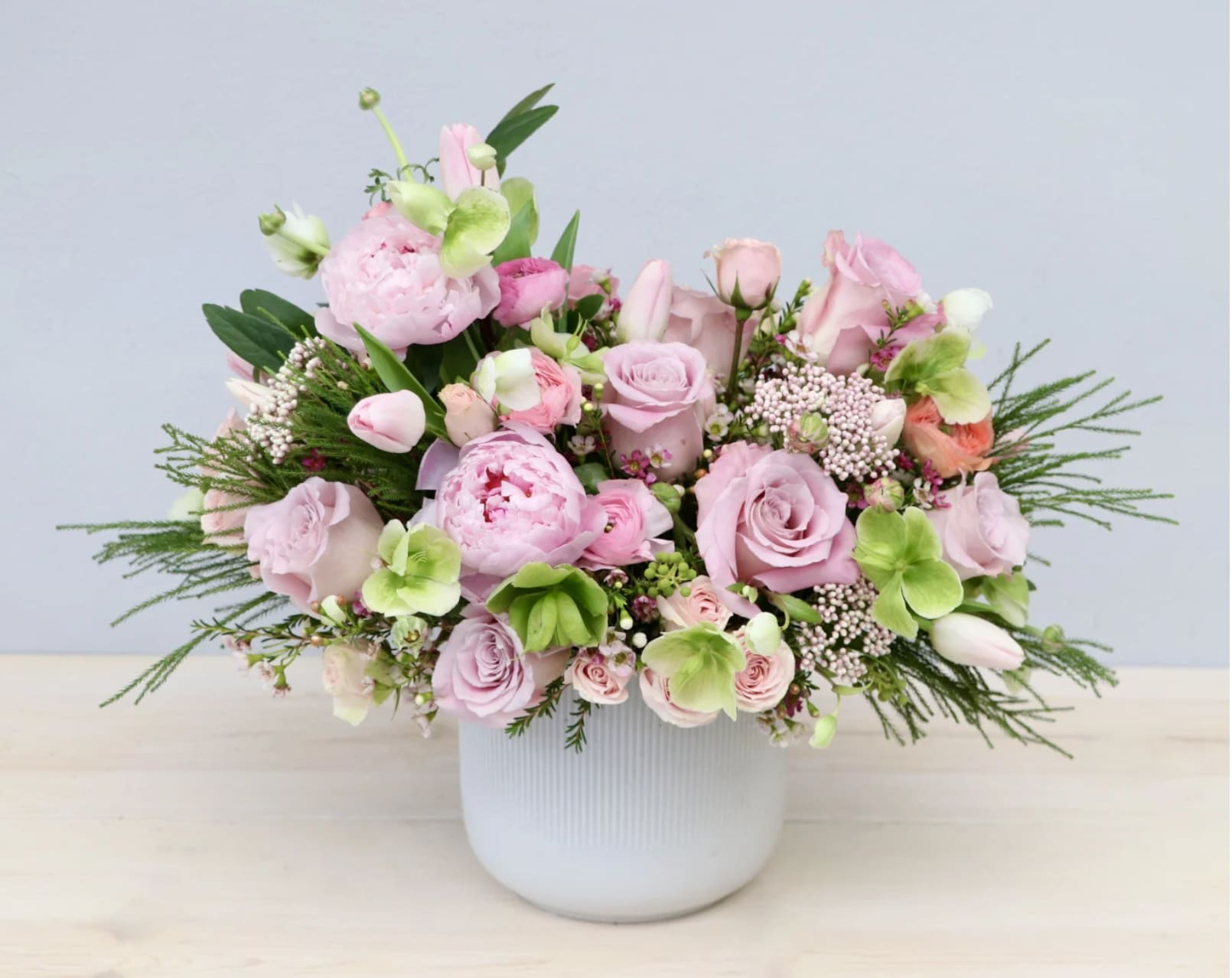 Low white vase filled with pink roses, peonies, tulips and green hydrangea blooms