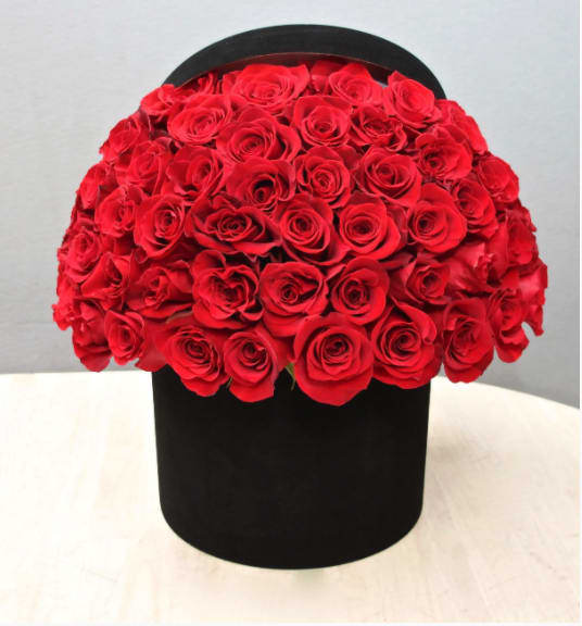 Large dome of red roses arranged in a round black hatbox-style container on a light table.