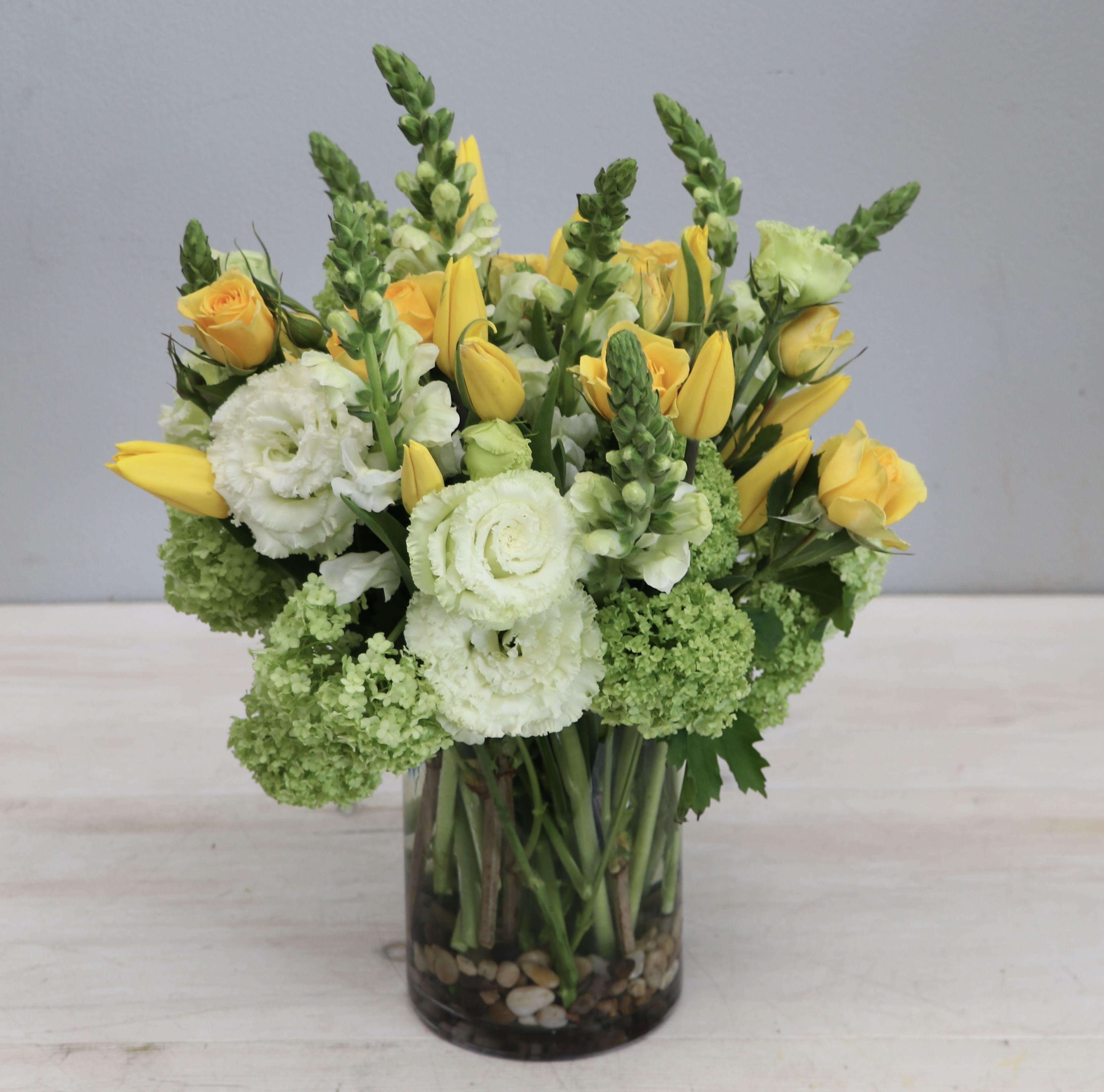 Meadow Morning - WeHo - This a vibrant and cheerful arrangement featuring yellow tulips and fresh green viburnum. White hydrangea and lisianthus bring balance to the bouquet, creating a visual harmony between the colors. The name is fitting for the bright and playful feeling of the arrangement, which would make an excellent gift or centerpiece for a spring or summer event. Its bold colors and fresh scent will add a lively atmosphere to any room.